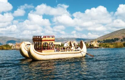 Bote tradicional de totora navegando en el Lago Titicaca, Puno, Perú, con cielo azul y paisajes naturales de fondo.